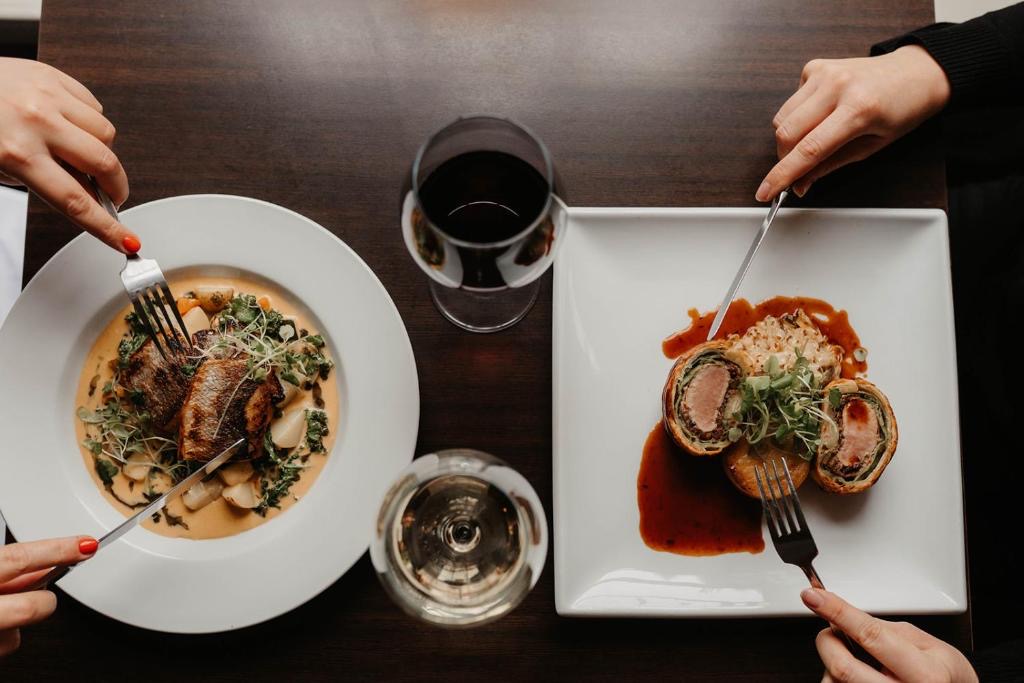 Seen from above: two plates of dinner, a glass of red and a glass of white, on a dark wooden table.