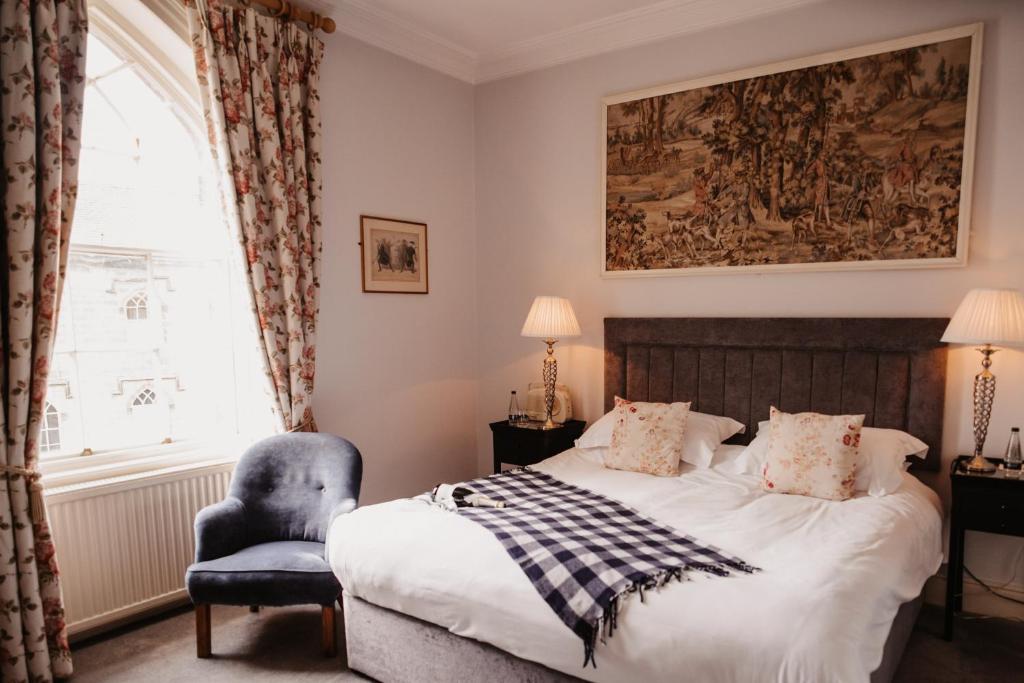 A bedroom with a blue velvet chair by a tall window looking onto the castle, and a tapestry above the bed.