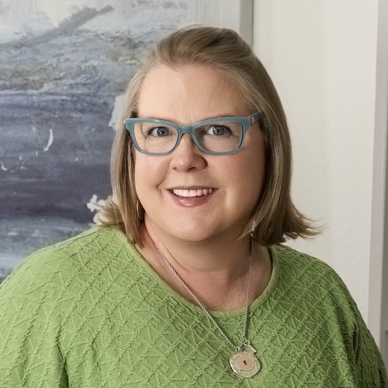 Stacy Earl, smiling, in teal glasses and a green top.